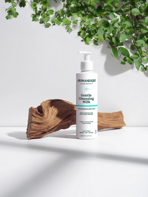 A pump bottle of Aromanesque Gentle Cleansing Milk placed on a white surface with a white background, surrounded by natural elements including a leaf and a piece of wood.